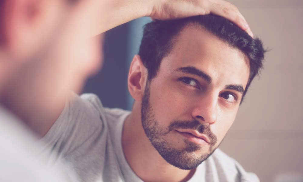 Soluciones para el cabello fino en hombres: Guía completa para un cabello fuerte y voluminoso 2 Hombre mirándose las entradas al espejo